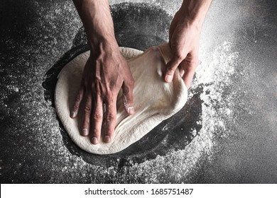 The process of preparing pizza, a person rolls out the dough with his hands. Horizontally close up.