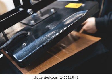 Process of printing image on clothes, heat press machine printing custom design on t-shirt and hoodie in fabric workshop, screen printing shirt, textiles and clothing, lithography and serigraphy