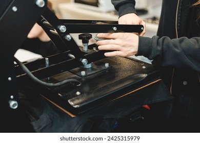 Process of printing image on clothes, heat press machine printing custom design on t-shirt and hoodie in fabric workshop, screen printing shirt, textiles and clothing, lithography and serigraphy
