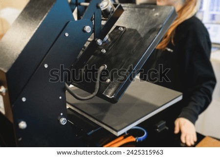 Process of printing image on clothes, heat press machine printing custom design on t-shirt and hoodie in fabric workshop, screen printing shirt, textiles and clothing, lithography and serigraphy