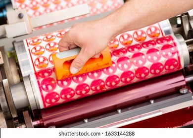 Process of removing possible dust debris on polymer plate in magenta print tower station with sticky roll on flexographic printing press. Dirt removing from photopolymer in flexo print machine.