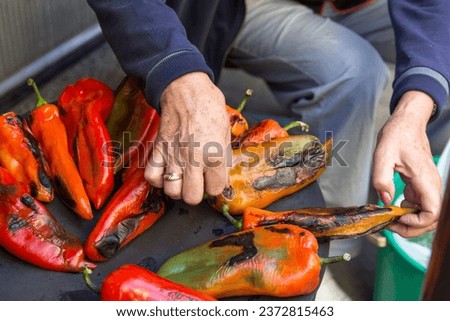 The process of roasting peppers on the wood fired stove outdoors in the yard. The woman's hands are turning the peppers to prevent burning. Concept of preparing ajvar on an autumn day