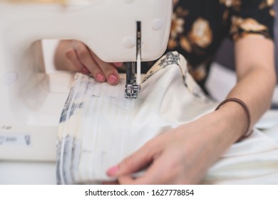 Process Of Sewing The Curtains At Home, Close Up Of Curtain Tape On The Sewing Machine, Hemming, Tailoring, Repairing And Stitching Cloth And Dress, With The Hand Of Female Dressmaker In Background
