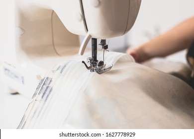 Process Of Sewing The Curtains At Home, Close Up Of Curtain Tape On The Sewing Machine, Hemming, Tailoring, Repairing And Stitching Cloth And Dress, With The Hand Of Female Dressmaker In Background
