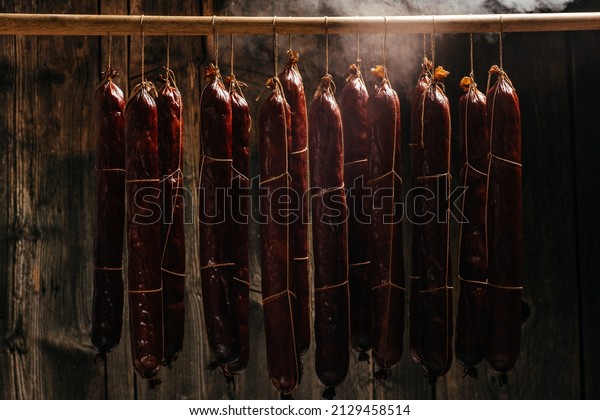 Process of smoking sausage hang in a cupboard\
with smoke. Clouds of smoke rise up and envelop the sausages\
hanging in a row. Long banner\
format,