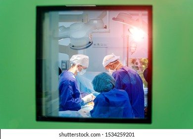 Process Of Surgery Operation Using Medical Equipment. Group Of Surgeons In Operating Room With Surgery Equipment. Medical Background. View From The Window To The Operating Room.