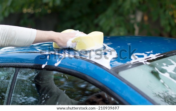 The process of washing a blue car\
with the help of shampoo and yellow sponges in the\
yard