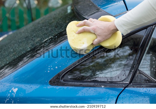 The process of washing a blue car\
with the help of shampoo and yellow sponges in the\
yard