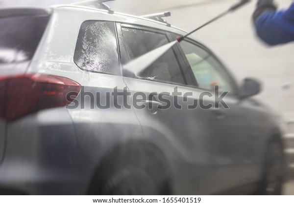 Process of\
washing the silver grey car in the carwash, concept of manual car\
wash with pressurized water, worker washing car\'s alloy wheels on a\
car wash, detail view of wash foam\
water.