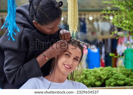 Process of weaving long African braids by a dark-skinned girl hairdresser. Hairstyle in the style of hippies, services of a modern beauty salon for a pretty young woman