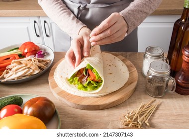 the process of wrapping a flatbread with vegetables and chicken pieces, pricking with a wooden skewer. a close angle on a wooden table - Powered by Shutterstock