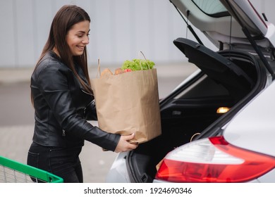 A process of young attractive woman taking groceries from a supermarket from the trolley to car truck. Food shopping during quarantine. Happy smiled woman - Powered by Shutterstock