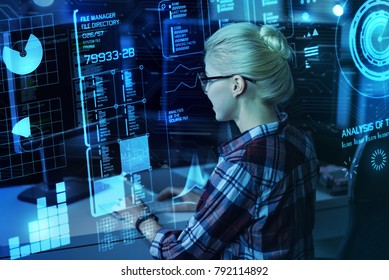 Processing information. Smart experienced enthusiastic programmer feeling interested while sitting in front of a big modern transparent screen and analyzing the latest statistics of cyber attacks