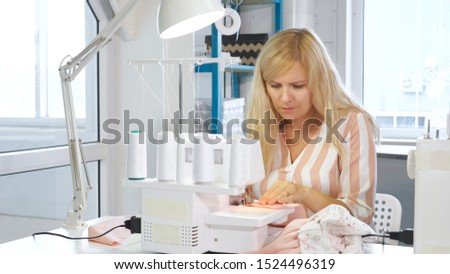 Processing tissue overlock. Seamstress working at sewing workshop sews on overlock cloth edges. Clothing manufacture. Stitches seams with straight stitch and finish them with serger overlock stitch.