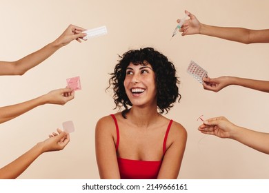 Pro-choice woman choosing the right form of contraception for her body. Happy young woman smiling cheerfully while surrounded by hands holding different hormonal and non-hormonal contraceptive methods