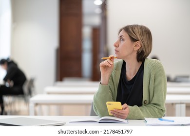 Procrastination concept. Thoughtful female mature student looking away while studying in library, pensive lost in thoughts middle-aged woman adult learner disinterested in study looking into distance - Powered by Shutterstock