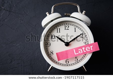 Procrastination and delay concept. Sticky note with word later on the white alarm clock. Urgency time