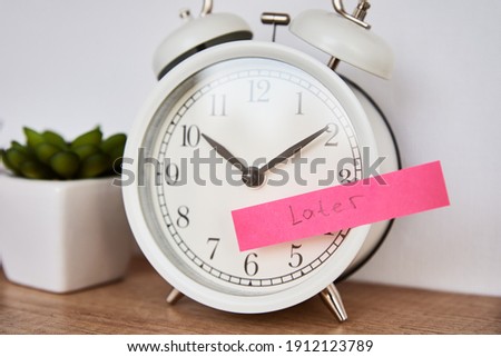 Procrastination and delay concept. Sticky note with word later on the white alarm clock. Urgency time