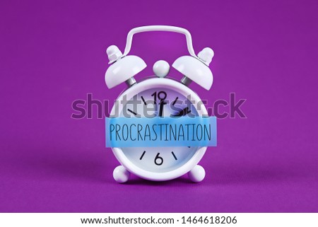 Procrastination, delay and urgency concept. White alarm clock with text procrastination.