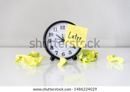 Procrastination delay and urgency concept with word later on sticky paper over white alarm clock and crumpled paper ball, bad time management.