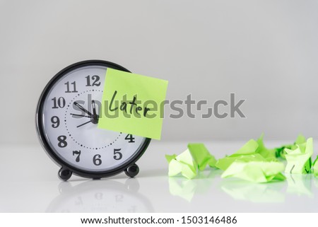 Procrastination delay and urgency concept with word later on green sticky paper over white alarm clock and crumpled paper ball, bad time management.