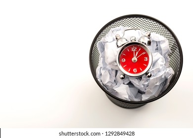 Procrastination Is The Enemy Of Productivity And Stop Wasting Time Concept Theme With A Clock In A Black Waste Basket Or Rubbish Bin Next To Crumpled Paper Isolated On White Background With Copy Space