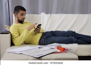 Procrastination. A Man Lying On The Couch And Looking At The Phone. He Does Not Want To Work.