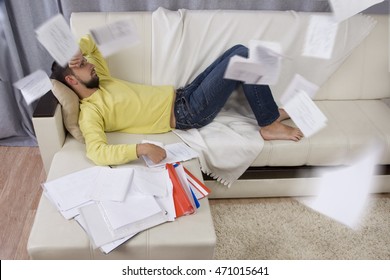 Procrastination. Man Lying On The Sofa. He Does Not Want To Work. Working Papers Flying In All Directions