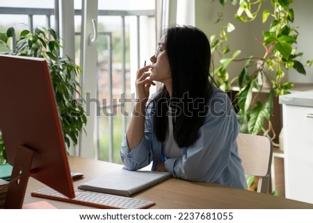 Procrastination in online learning. Dreamy Asian student girl getting distracted while studying remotely at home, sitting at desk with computer looking out window, having no motivation to study