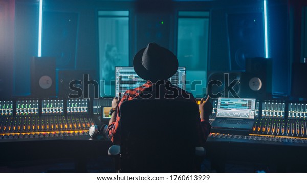 Producer, Audio Engineer Uses Control Desk for
Recording New Album Track in Music Record Studio, in the Soundproof
Room Musician, Artist, Performer Sings a Song from New Album. Back
View