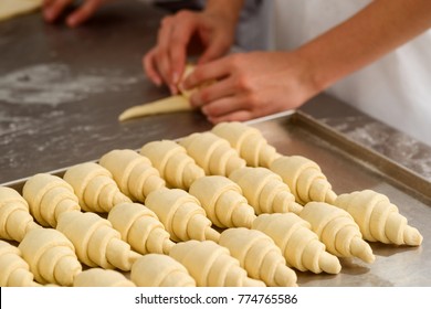 Producing classic croissants at the bakery shop. Woman is rolling dough into rolls for further baking. French pastry goods.