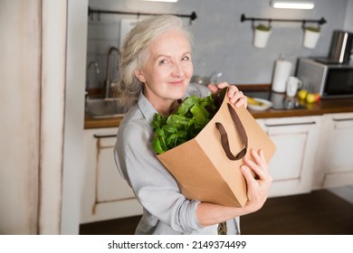 product delivery. healthy nutrition.  elderly woman with a bag of green lettuce in the kitchen at home. Senior lifestyle - Powered by Shutterstock