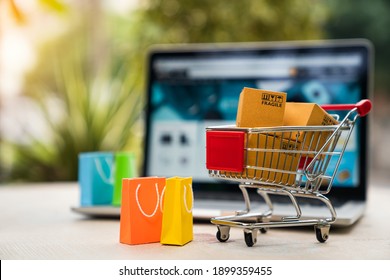 Product package boxes in cart with shopping bag and laptop computer with blurred web store shop on screen for online shopping and delivery concept