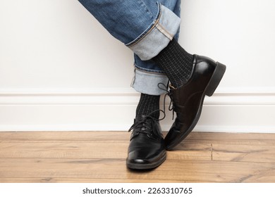 Product photo of men's footwear. This is a close up on a man wearing black leather dress shoes, black dress socks and blue jeans. 