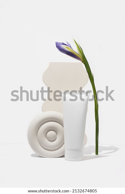 Product photography with flowers\
and geometric props. White cosmetic cream tube on white\
background