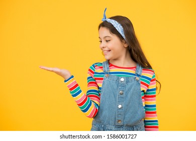 Product Presentation. Kid Happy Smiling Face Show Something On Open Palm Copy Space Yellow Background. Girl Demonstrate Product. Advertisement Concept. Promoting Product For Kids. Launching Product.