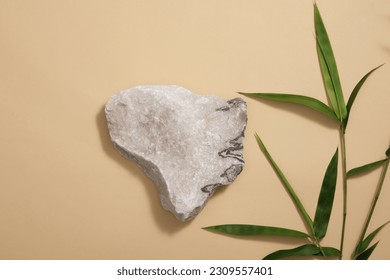Product and promotion concept for advertising - a small gray stone as an empty podium on brown background with green bamboo leaves. Blank space for cosmetic product presentation. Stock Photo