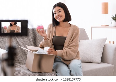 Product Review. Asian Young Woman Vlogger Holding Cream, Showing Cosmetics Products, Recording Video For Her Beauty Blog On Camera At Home, Female Influencer Shooting Brand Advertising Promo