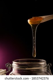 Product Shot Of A Spoon Dripping Honey Into A Jar Isolated On A Black Background. 