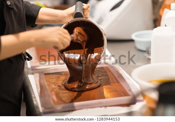 production, cooking and\
people concept - confectioner filling mold with chocolate at\
confectionery shop