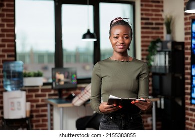 Production Department Team Leader Standing In Digital Art Studio. Confident Creative Art Designer Standing In Office Workspace Having Clipboard Paperwork Documentation While Smiling At Camera.