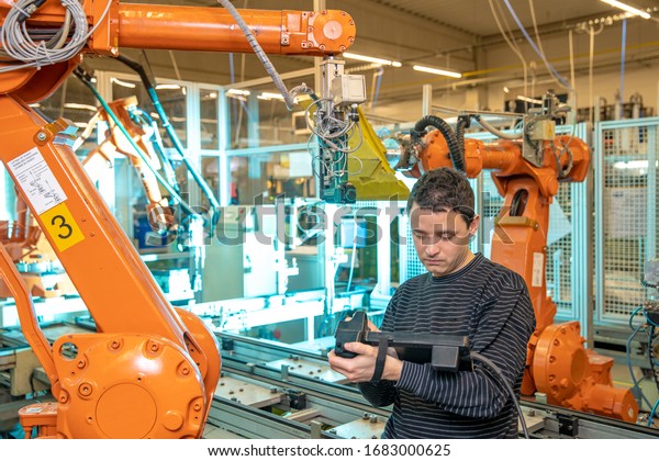 production engineer programs the robotic arms on\
the production line in a\
factory