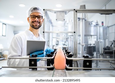 Production Line Worker Or Technologist Standing By The Automated Conveyor Machine With Liquid Soap Products And Cleaning Chemicals.