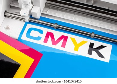 Production Making CMYK Sticker With Plotter Cutting Machine On Cyan Blue Colored Vinyl Film Advertising Industry Diy Design On Concept Background.