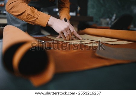 Production process. Young focused experienced master craftsman makes leather goods at his workplace.