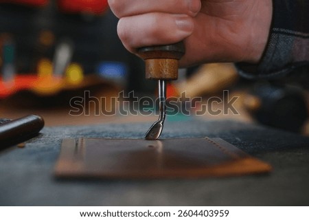 Production process. Young focused experienced master craftsman makes leather goods at his workplace.