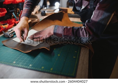 Production process. Young focused experienced master craftsman makes leather goods at his workplace.