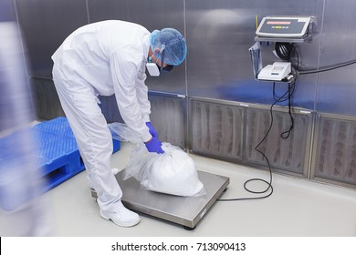 Production room in the medical laboratory. The specialist in the protected clothing and mask weighs the produced medical preparations on special scales.