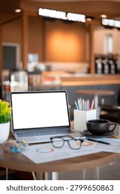A productive remote work setup in a cozy coffee shop featuring an open laptop mockup, stationery, and charts, ideal for freelance and business concepts.