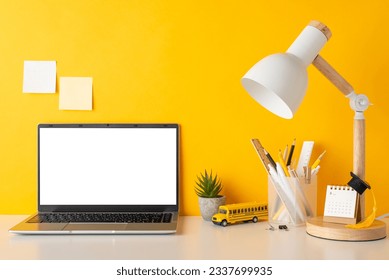 Productive study setup. Side view photo of desk with stationery, calendar, academic cap, flowerpot, open laptop, lamp, school bus toy, sticky notes on yellow wall background. Copy space for text - Powered by Shutterstock